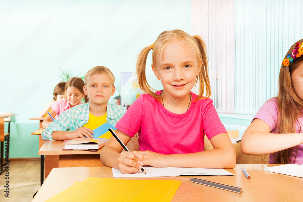 Kids sitting at table in classroom and writing Kids sitting at table in classroom and writing