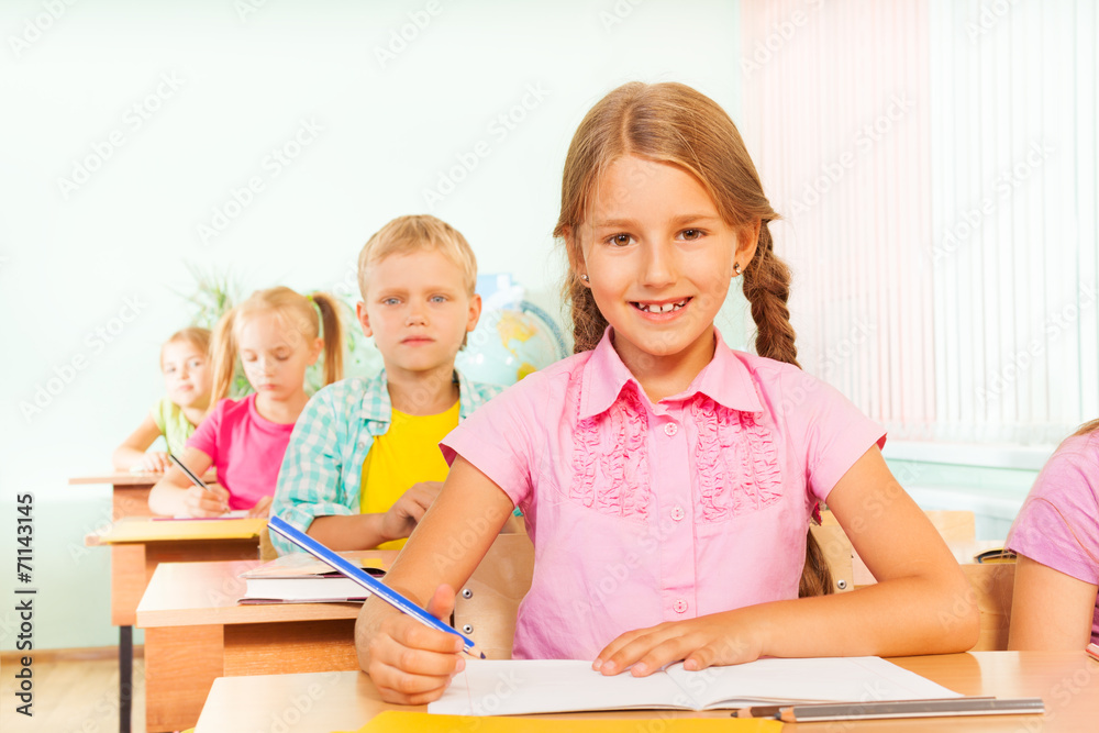 Cute girl smiles, sits at desk and writes Cute girl smiles, sits at desk and writes