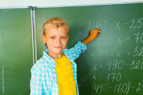 Boy with chalk stands near blackboard and looking