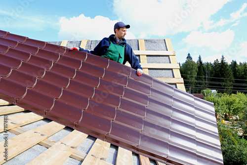 Worker puts the metal tiles on the roof of a wooden house © kingan
