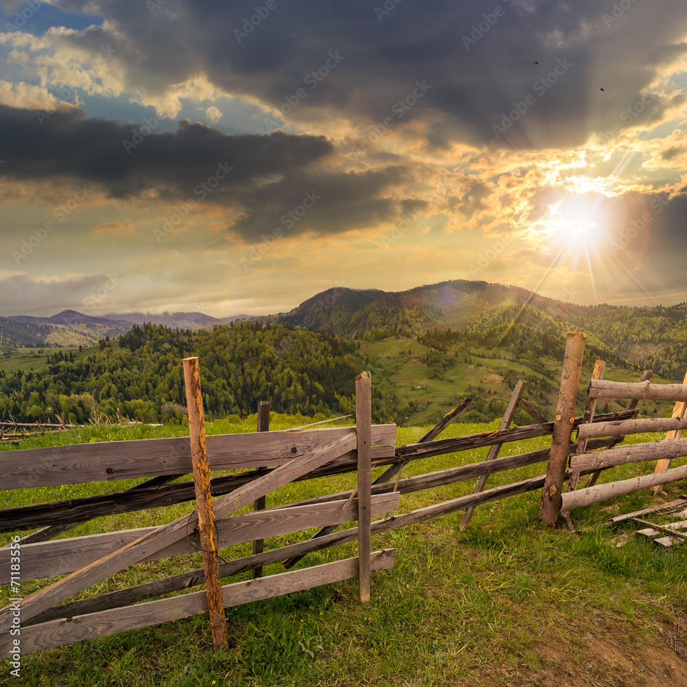 Fototapeta premium fence on hillside meadow in mountain at sunset