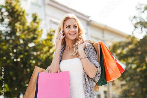 Young blond woman with shopping bags calling by mobile phone