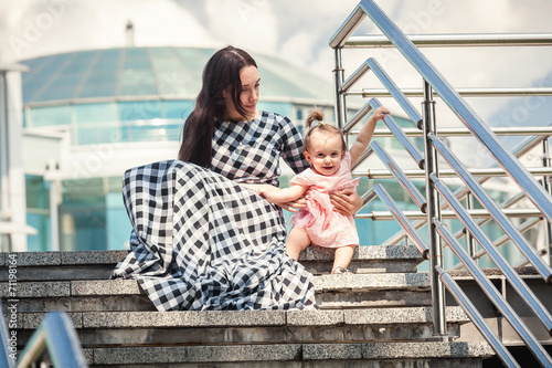 young mother and baby girl sitting on stairs on street
