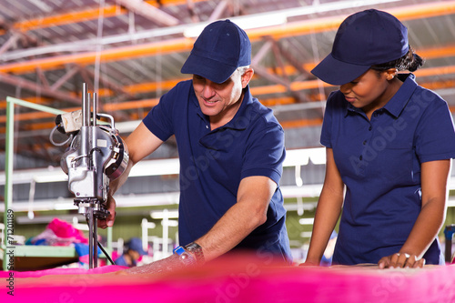 senior textile worker teaching new employee about cutting fabric
