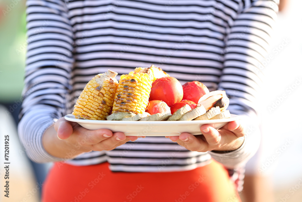 женщина на тарелку с пастой добавляет овощи гриль