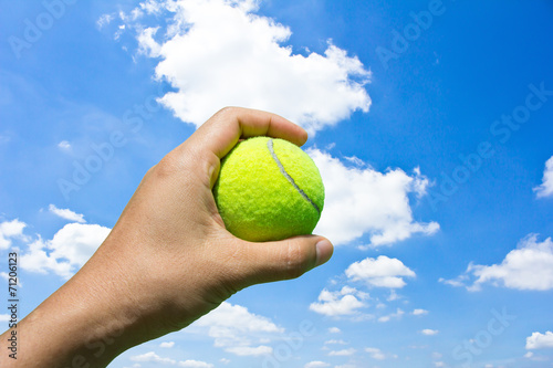 Hand holding tennis ball on blue sky background © torsak
