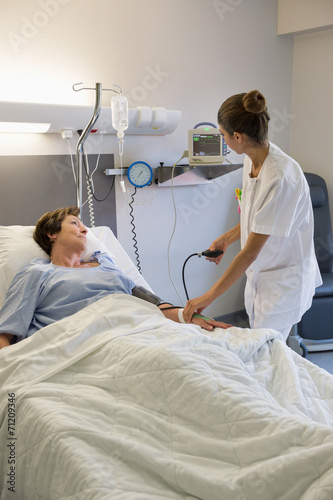 Female nurse checking patient's blood pressure on hospital bed