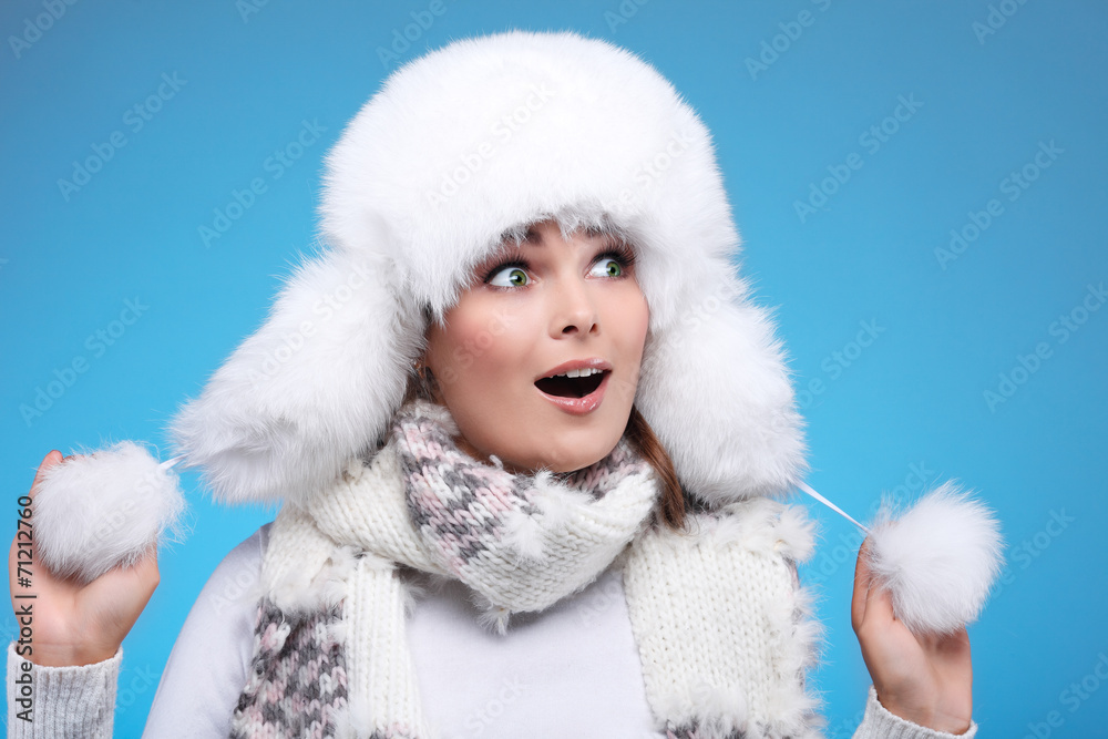 Beautiful girl in a white fur cap and warm clothes on a blue Beautiful girl in a white fur cap and warm clothes on a blue