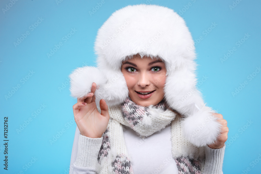 Beautiful girl in a white fur cap and warm clothes on a blue Beautiful girl in a white fur cap and warm clothes on a blue