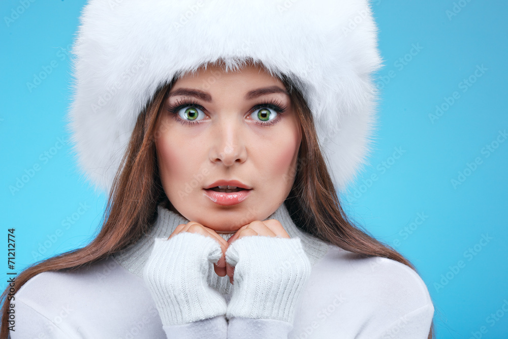 Beautiful girl in a white fur cap and warm clothes on a blue Beautiful girl in a white fur cap and warm clothes on a blue