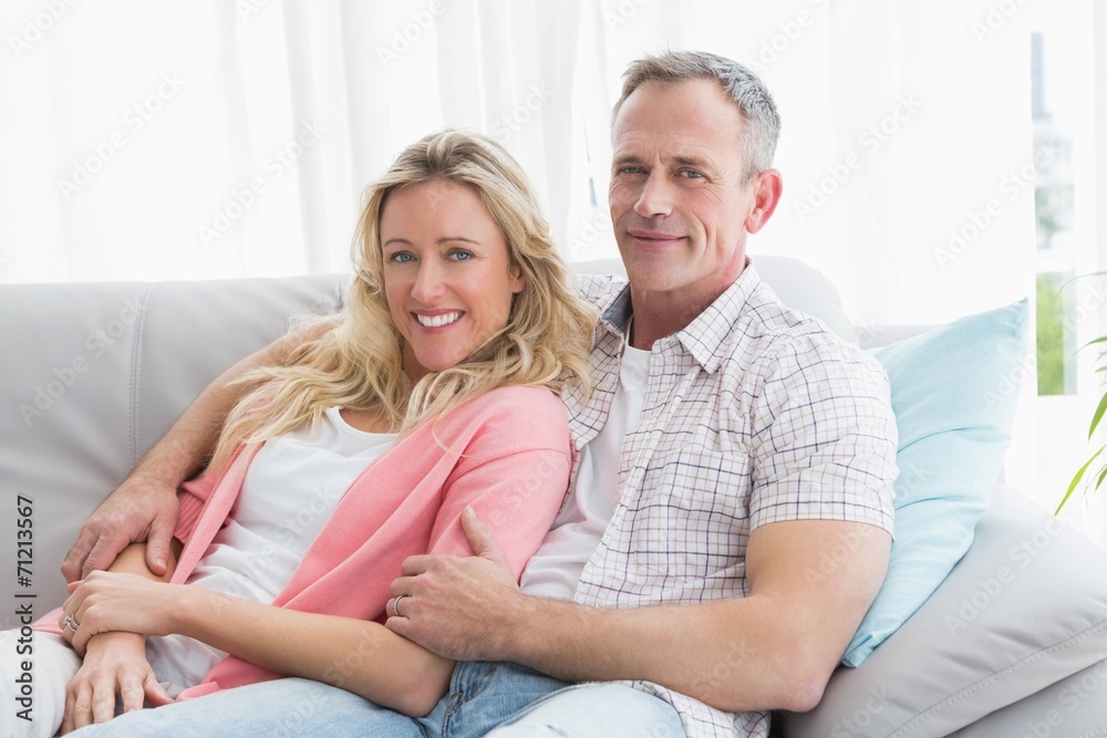 Happy couple relaxing on the couch smiling at camera Happy couple relaxing on the couch smiling at camera