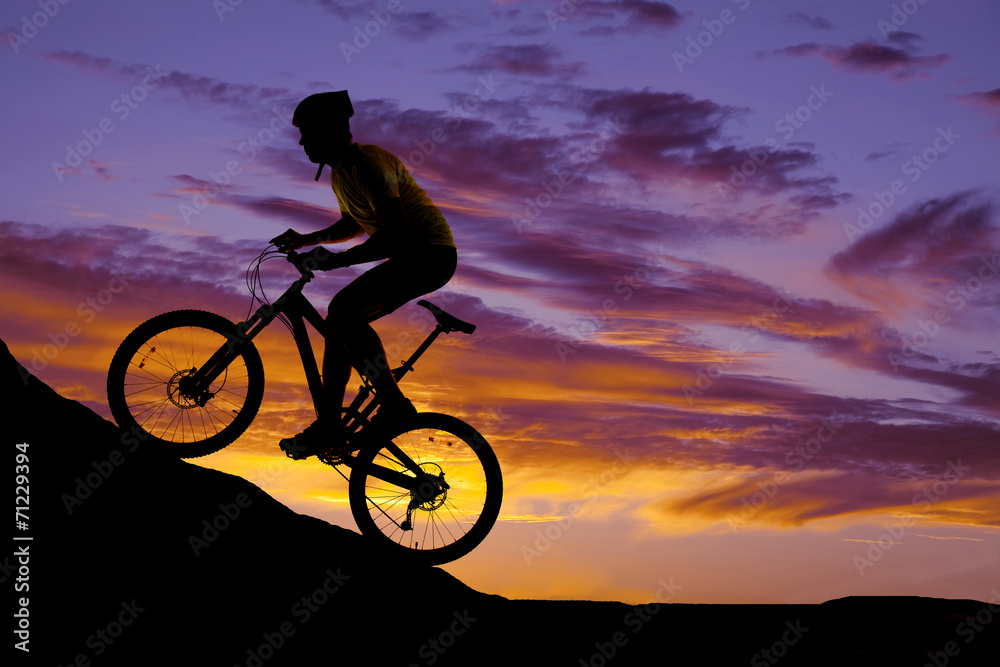 Fototapeta premium man riding a bike up a hill silhouette in the sunset