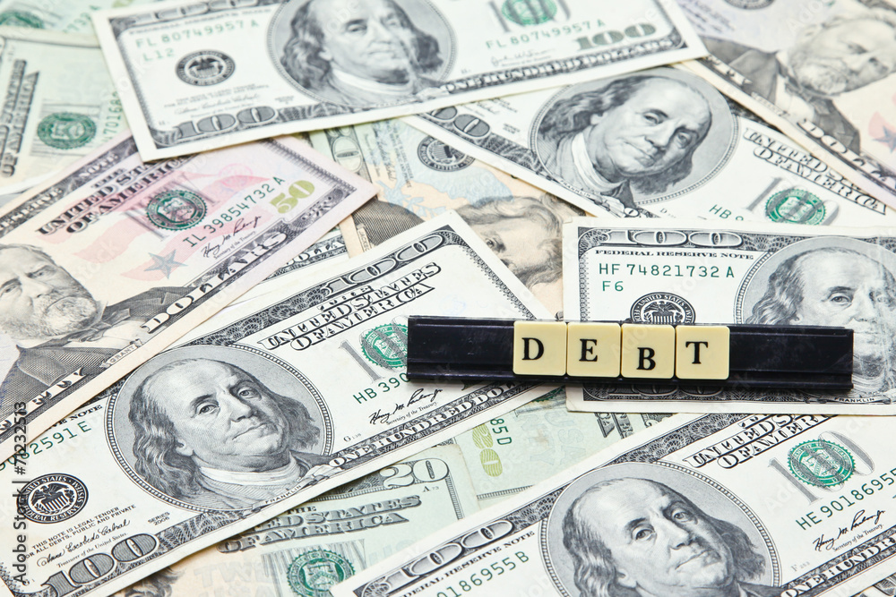 Word debt on pile of US dollar banknotes Word debt on pile of US dollar banknotes