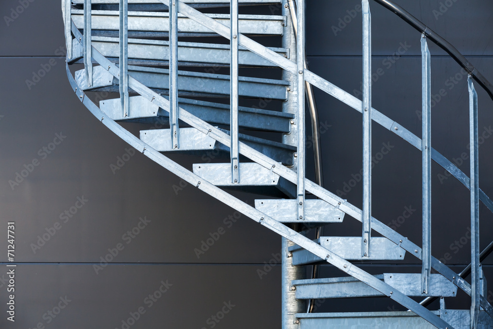 Fragmetn of modern metal spiral staircase above dark gray wall - obrazy, fototapety, plakaty 