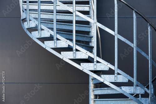 Fragmetn of modern metal spiral staircase above dark gray wall