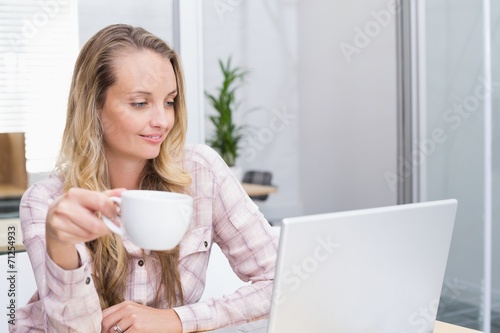 Cheerful businesswoman using her notebook holding a cup