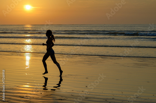 Silhouette of woman jogger running on sunset beach