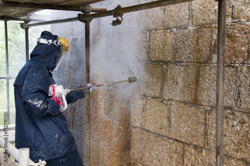 Worker cleans ancient stone wall with high pressure washer from