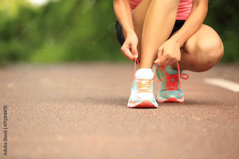 woman runner tying shoelace on trail woman runner tying shoelace on trail
