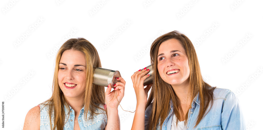 Friends talking through a tin phone over white background Friends talking through a tin phone over white background