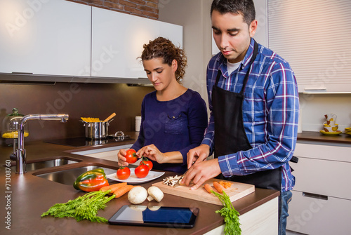 Couple in home kitchen looking recipe with a electronic tablet