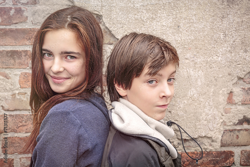 siblings back to back in front of an old brick wall siblings back to back in front of an old brick wall
