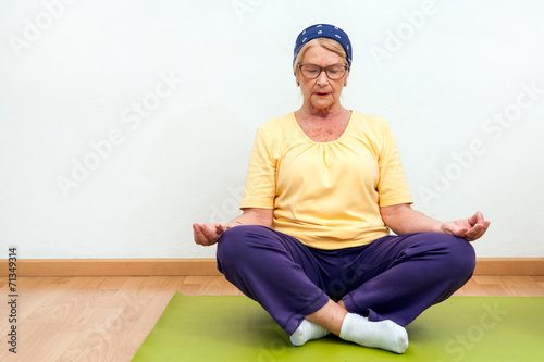 Elderly woman practising yoga in gym.
