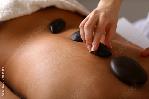 Bright young woman enjoying a back massage with hot stone in a