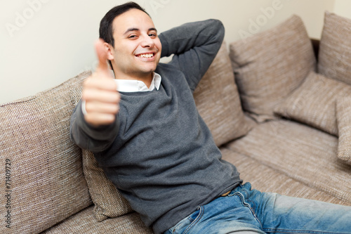 Young guy sitting on sofa showing OK sign