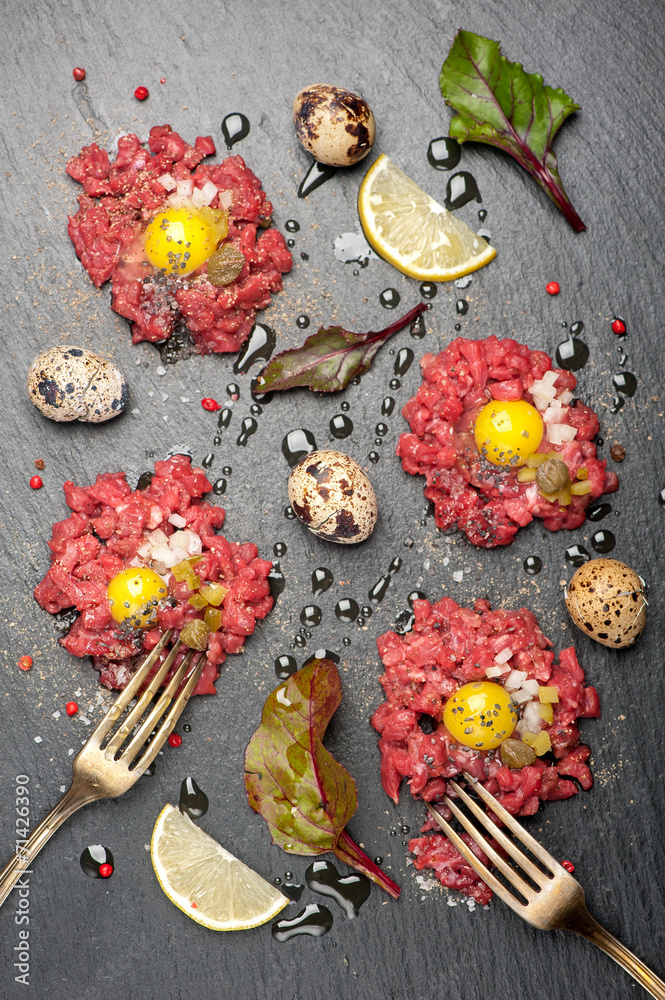 Beef tartare with egg, capers and onions on dark background