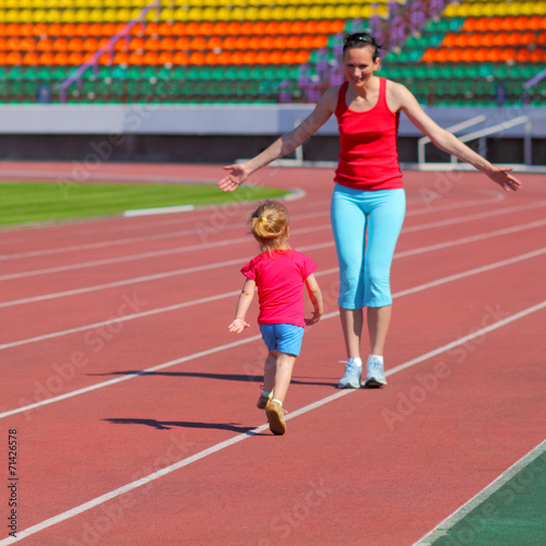 Mother and little daughter are running in the stadium.