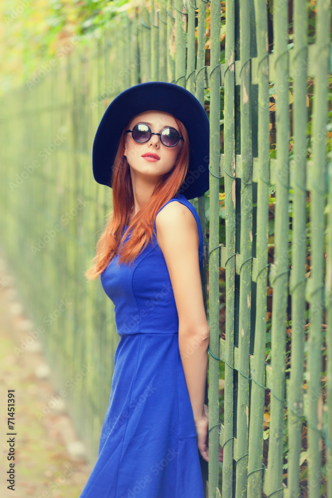 Redhead girl in sunglasses near fence in Versailles garden