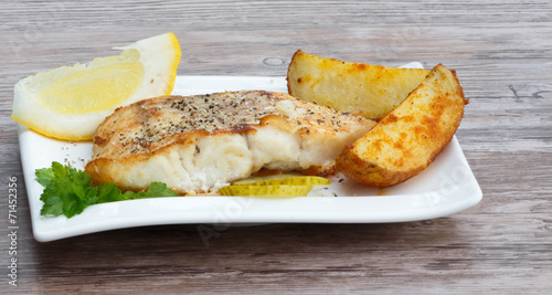 White fish with potato wedges on white plat, wooden background photo