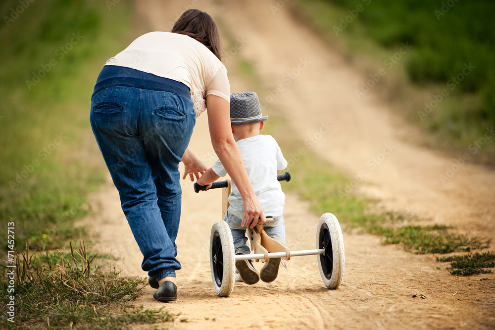 Obraz premium Mother with little boy on tricycle in nature