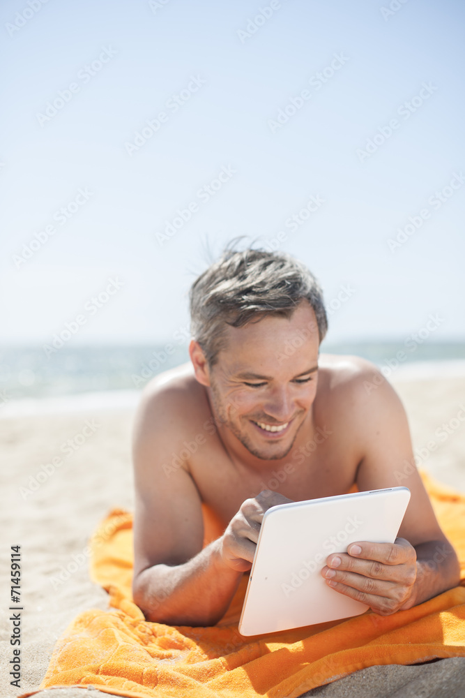 handsome man on the seaside lying on a beach towel to use a digi