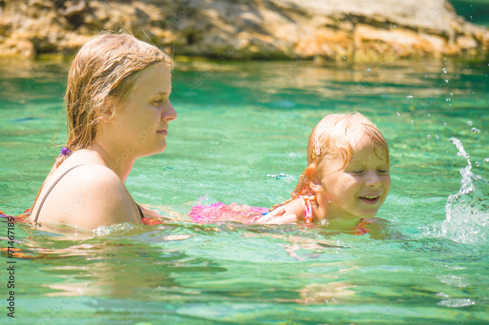 Young mother learn  daughter to swim in crystal clear laguna on