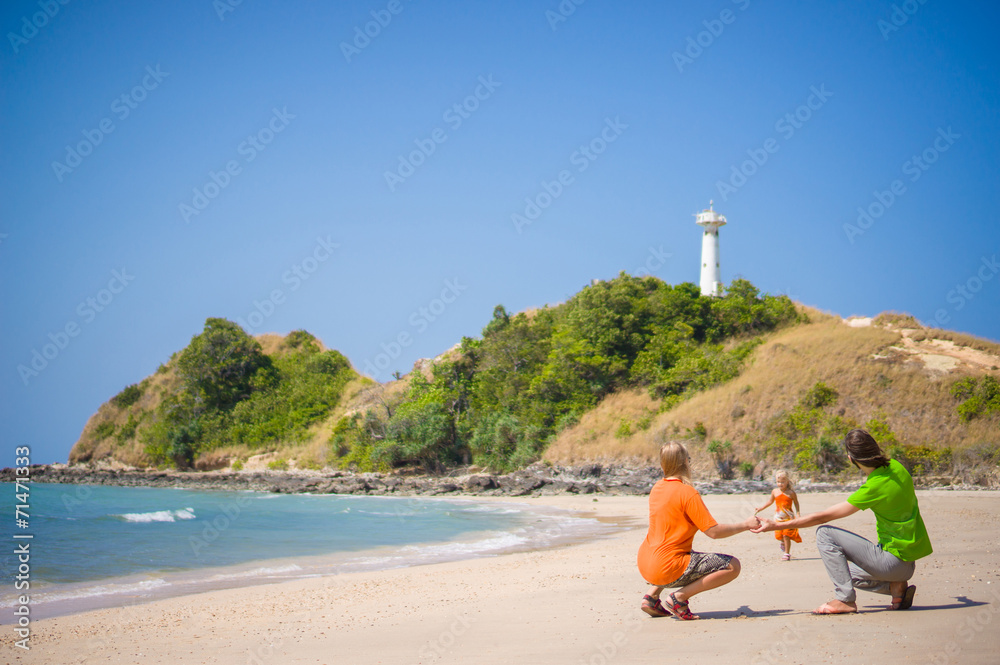 Mother, father walk along tropical beach holding hands with ligh