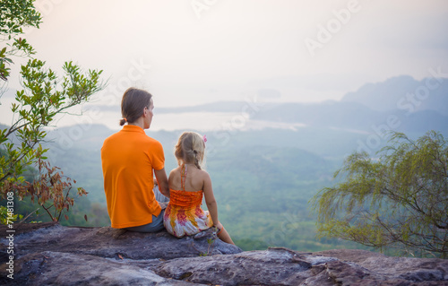 Father and daughter seat near cliff on the top of tropical islan