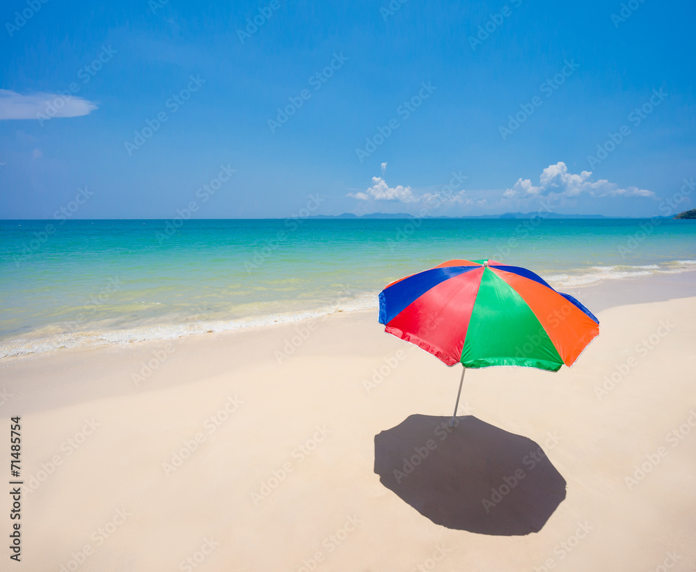 Rainbow color umbrella on empty ocean beach with waves