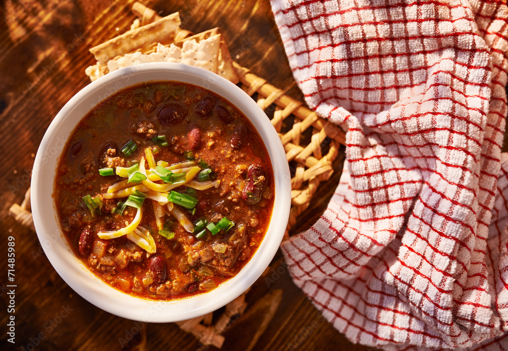 overhead photo of a bowl of chili with cheese and green onions - obrazy, fototapety, plakaty 