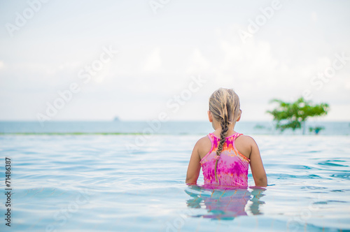 Adorable girl seat and look at ocean in pool at tropicapl beach