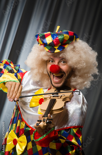 Funny clown plyaing violin against curtain