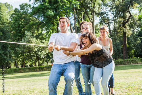 A large group of young people playing tug of war at the park