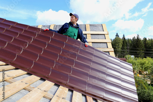 Worker puts the metal tiles on the roof of a wooden house