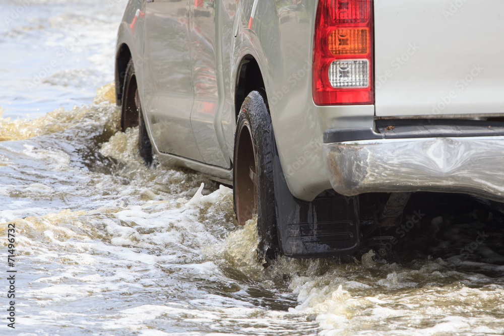 Car splashes through a large puddle on a flooded street - obrazy, fototapety, plakaty 