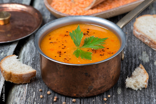 Spicy red lentil soup in a copper pot on a wooden table