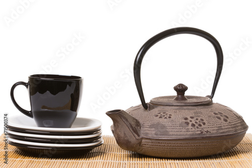 Black cup of tea on different saucers with iron teapot on wooden