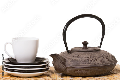 White cup of tea on different saucers and iron teapot on wooden