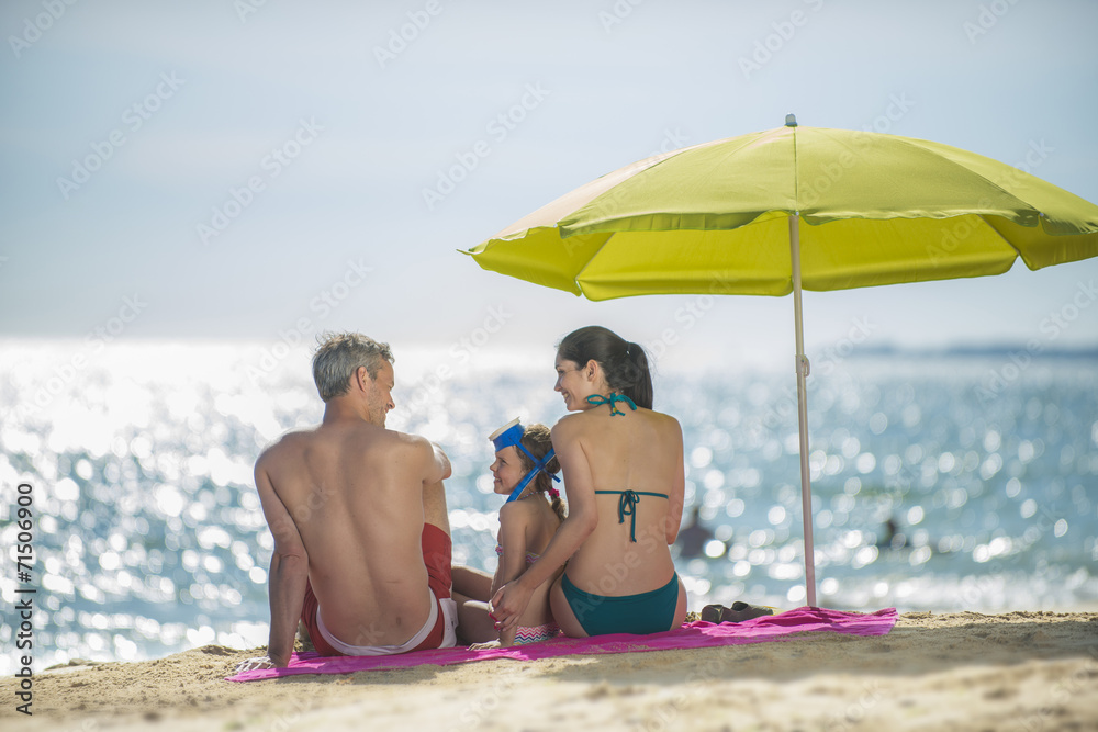 family in swimsuit  having fun at the beach  sitting under a bea