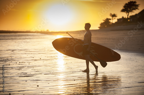 Photography silhouette of a man with his paddle board on the beach at sunset